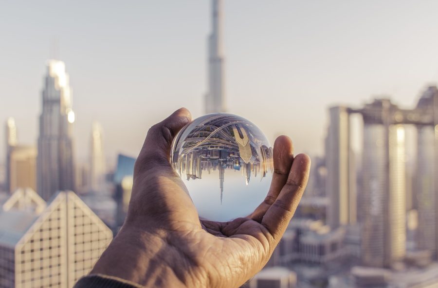 A closeup shot of a male hand holding a crystal ball with the reflection of the city